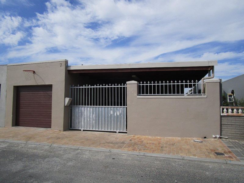 Front elevation of the property featuring a single garage, paved driveway, and secure metal gate entrance.