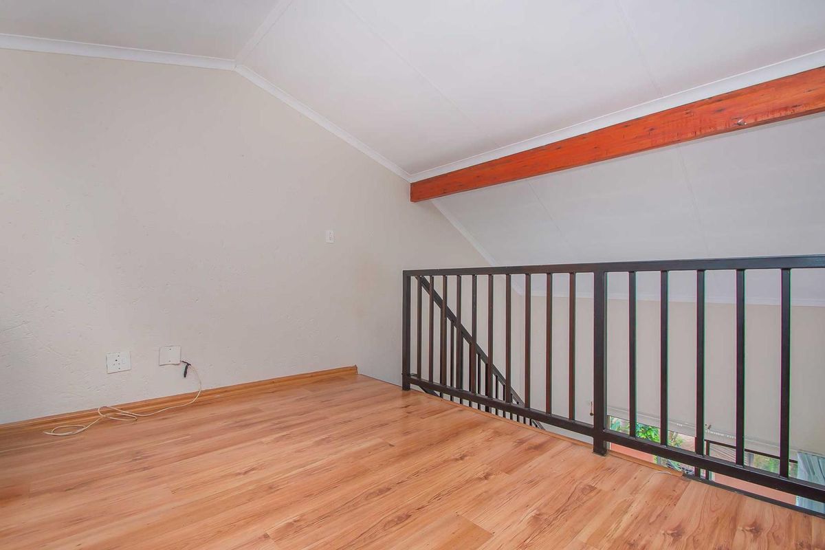 A loft-style bedroom area featuring laminate flooring, a vaulted ceiling with a decorative timber beam, and a black metal safety railing.