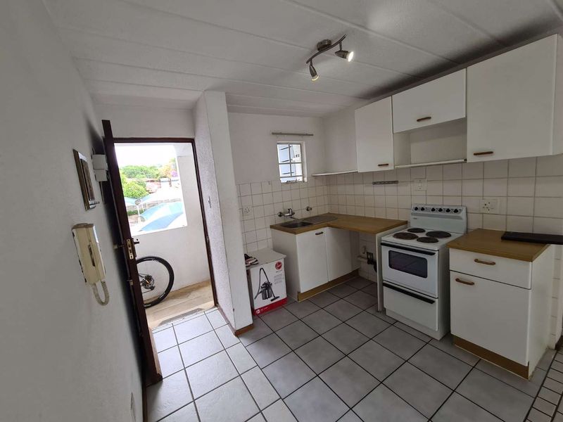 Functional kitchen featuring tiled flooring, white cabinetry, laminate countertops, and a freestanding electric stove, with direct access to an outdoor area.