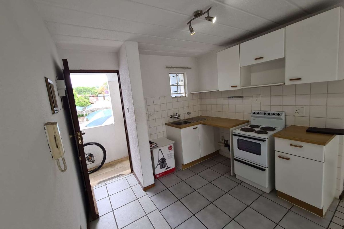 Functional kitchen featuring tiled flooring, white cabinetry, laminate countertops, and a freestanding electric stove, with direct access to an outdoor area.
