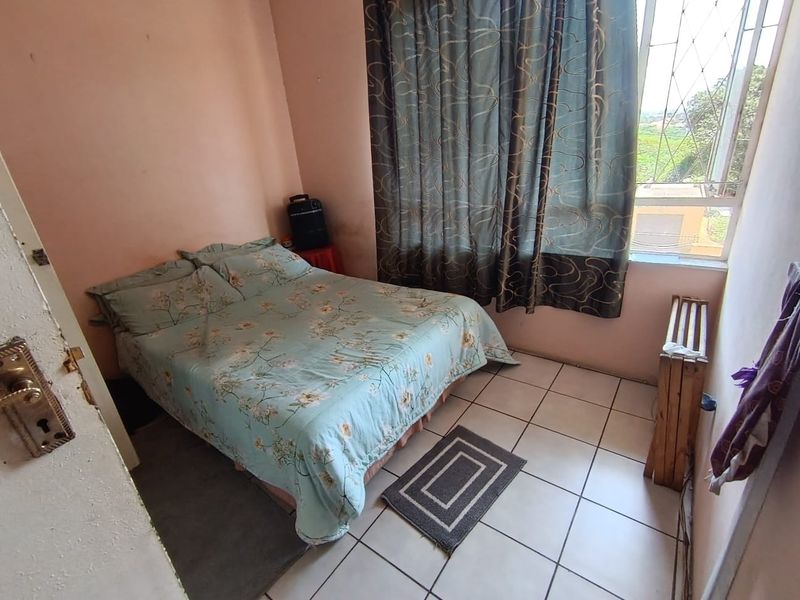 A compact bedroom featuring tiled flooring and a window with security bars, offering a functional space with potential for cosmetic updates.