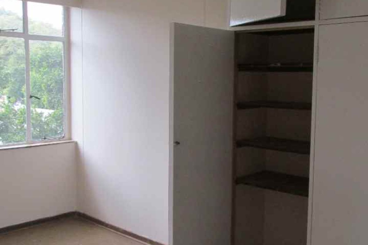 A vacant bedroom featuring built-in storage cupboards, tiled flooring, and a large window providing natural light.
