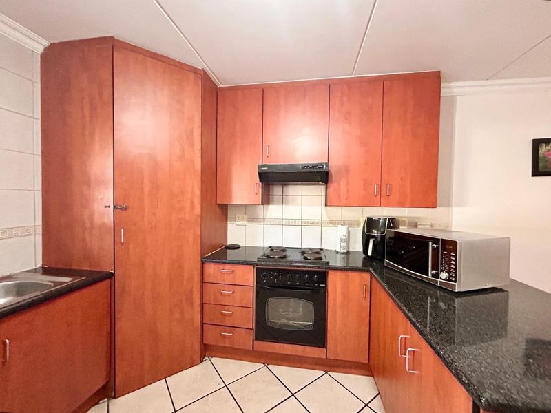 Functional kitchen featuring warm-toned built-in cabinetry, granite countertops, an electric hob, built-in oven, and a tiled backsplash.