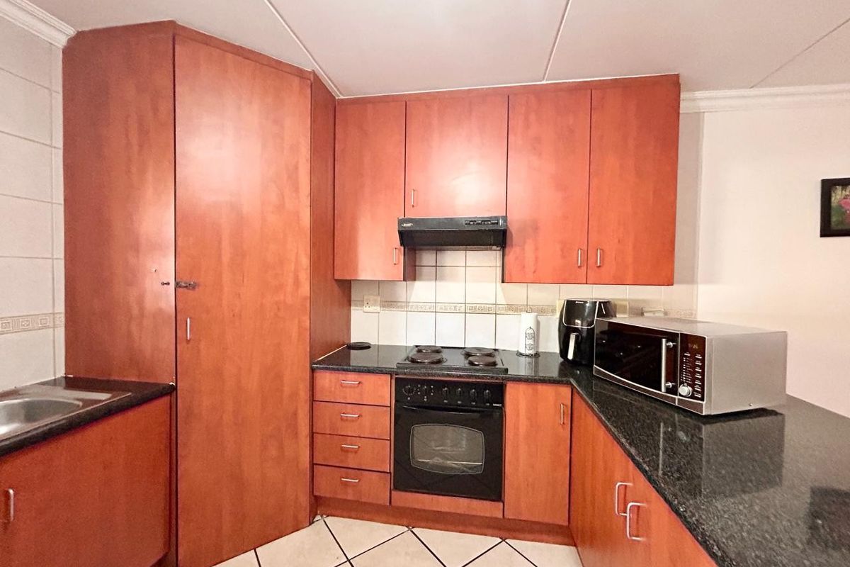 Functional kitchen featuring warm-toned built-in cabinetry, granite countertops, an electric hob, built-in oven, and a tiled backsplash.