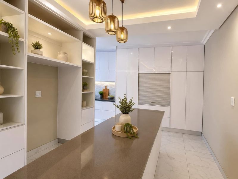 Modern kitchen featuring sleek white cabinetry, a large stone-topped island, integrated appliance storage, and elegant pendant lighting with recessed ceiling details.