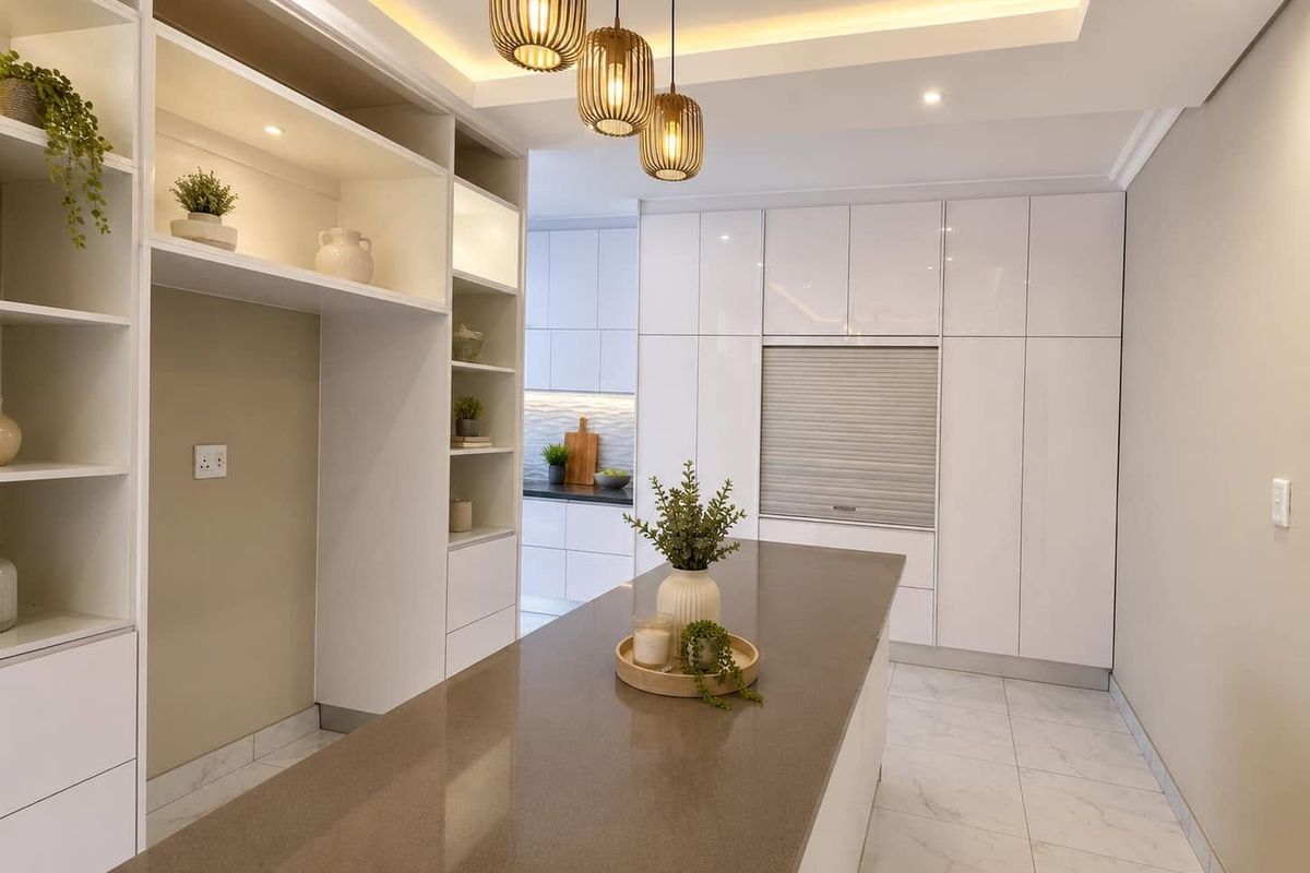 Modern kitchen featuring sleek white cabinetry, a large stone-topped island, integrated appliance storage, and elegant pendant lighting with recessed ceiling details.
