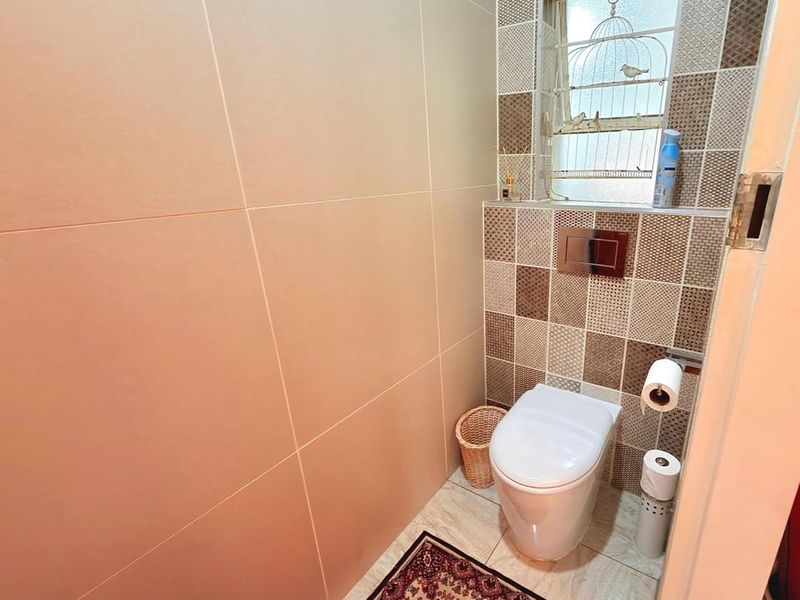 A compact guest bathroom featuring a wall-mounted toilet with a concealed cistern, finished with neutral wall tiles and decorative mosaic accents.
