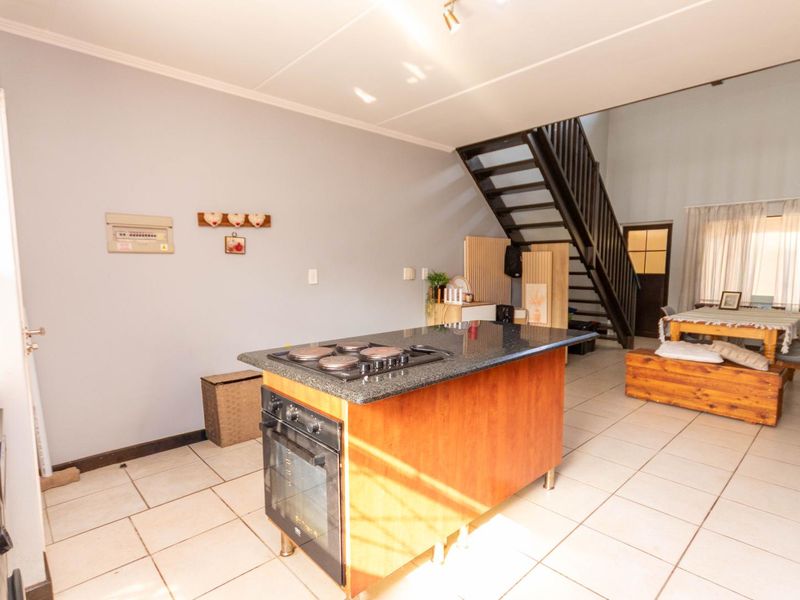 Open-plan living area featuring a central kitchen island with a built-in oven and hob, tiled flooring, and a staircase leading to the upper level.