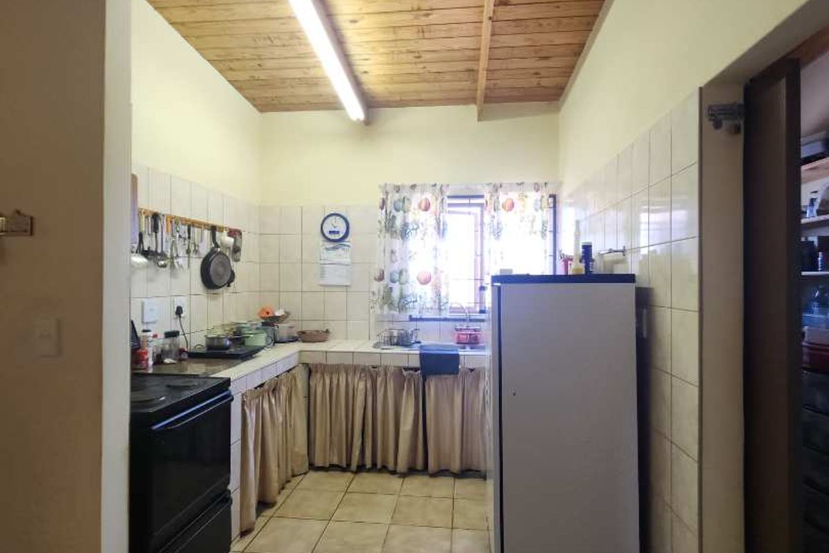 A functional kitchen featuring tiled flooring, a tiled splashback, a double sink, and an exposed timber beam ceiling with fluorescent lighting.