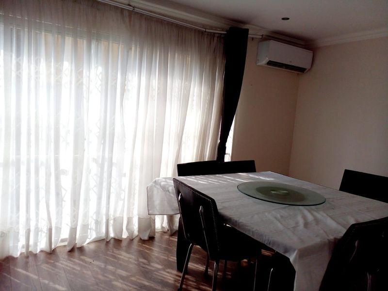 Dining area featuring laminate flooring, a wall-mounted split-system air conditioner, and large sliding glass doors providing natural light.