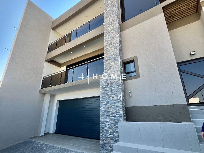 Modern multi-story residential facade featuring stone cladding, glass balustrades, an automated garage, and a paved entrance staircase.