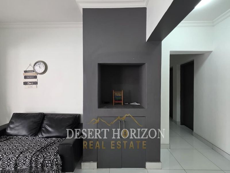 A living area featuring a dark grey accent wall with built-in cabinetry and a recessed niche, complemented by white walls and tiled flooring.