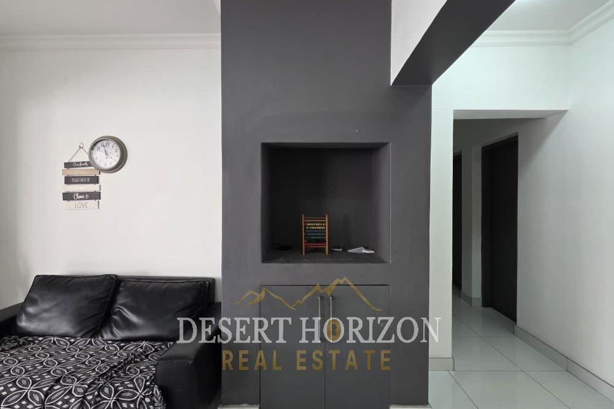 A living area featuring a dark grey accent wall with built-in cabinetry and a recessed niche, complemented by white walls and tiled flooring.