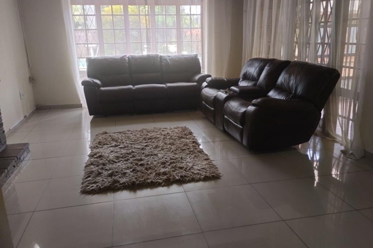 A spacious living room featuring large windows, sliding glass doors, and neutral tiled flooring, offering a bright and open living environment.