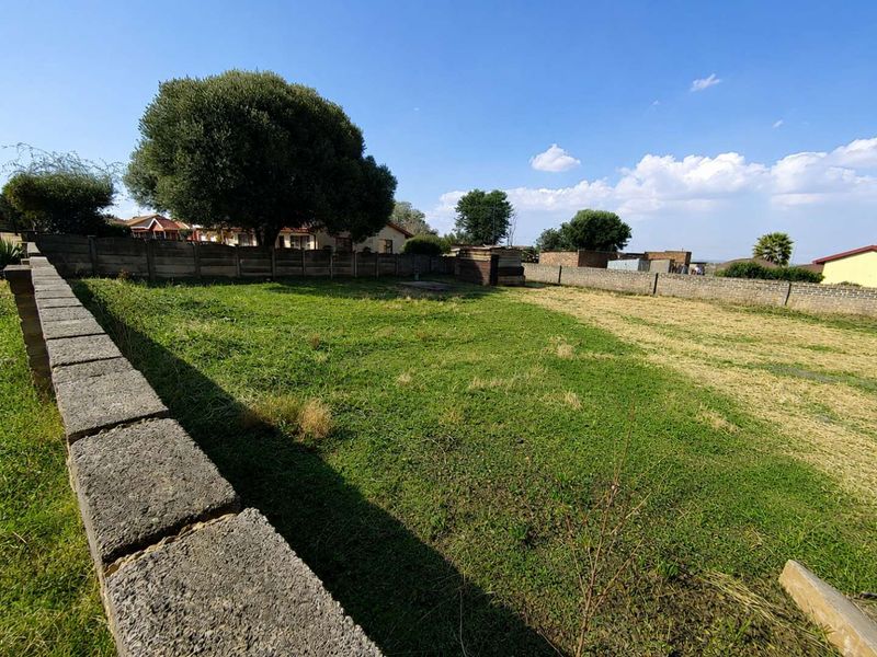A vacant residential plot featuring a grass lawn enclosed by perimeter concrete block walls.