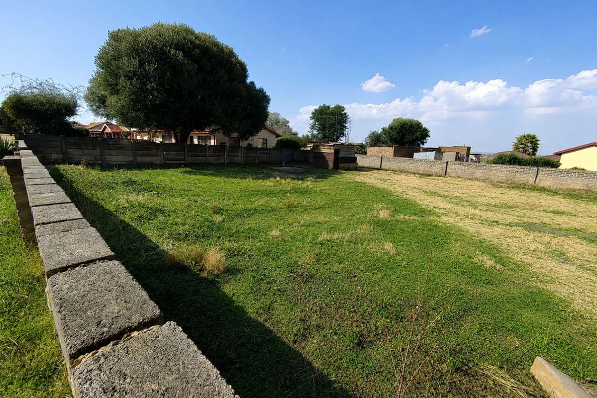 A vacant residential plot featuring a grass lawn enclosed by perimeter concrete block walls.