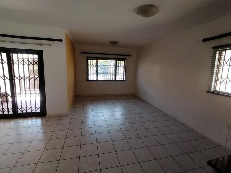 An empty, tiled living room featuring security gates on the sliding door and windows, offering a blank canvas for interior design.