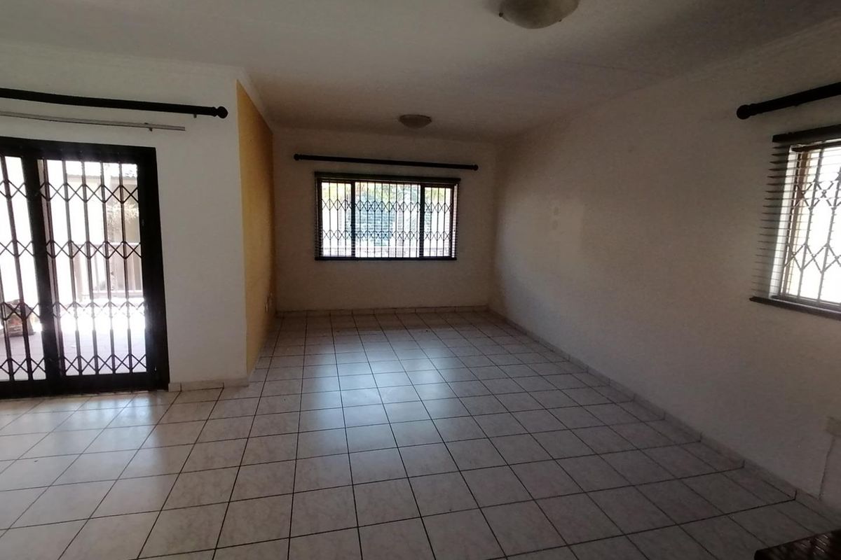 An empty, tiled living room featuring security gates on the sliding door and windows, offering a blank canvas for interior design.