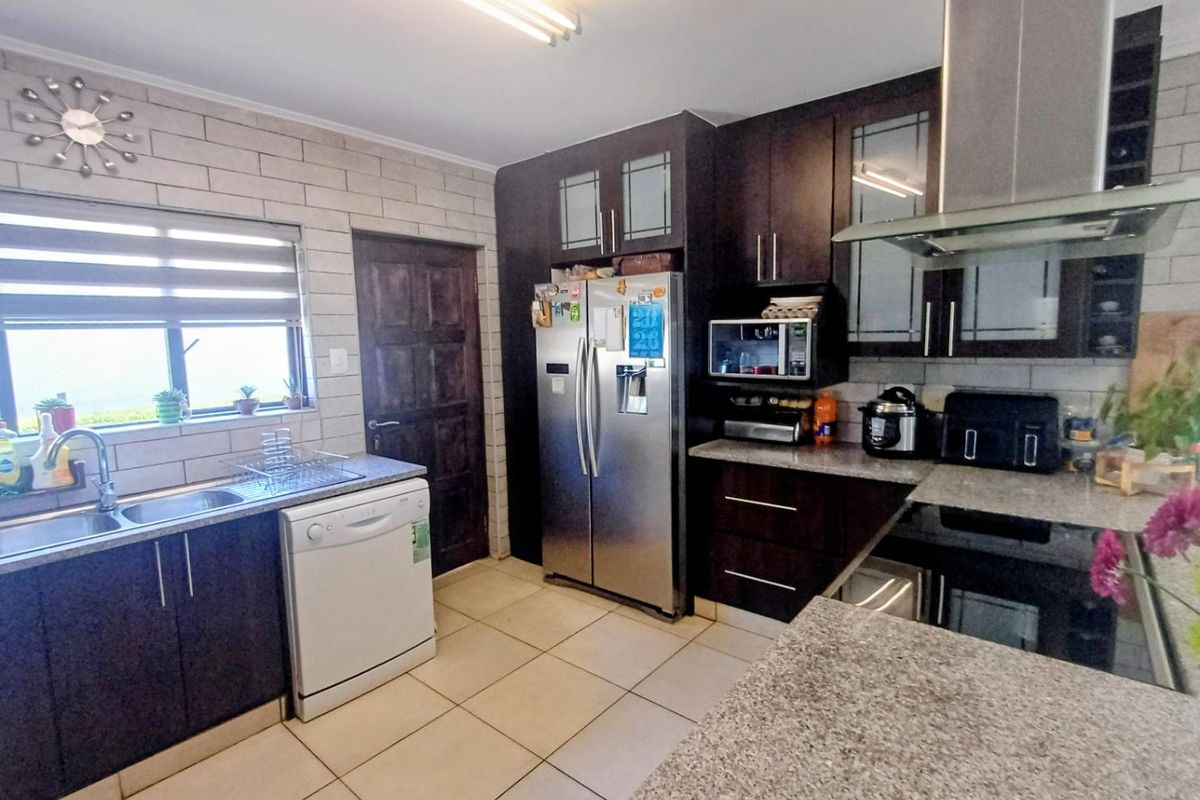 A functional kitchen featuring dark wood cabinetry, granite countertops, a stainless steel extractor fan, and tiled flooring with a neutral tiled splashback.