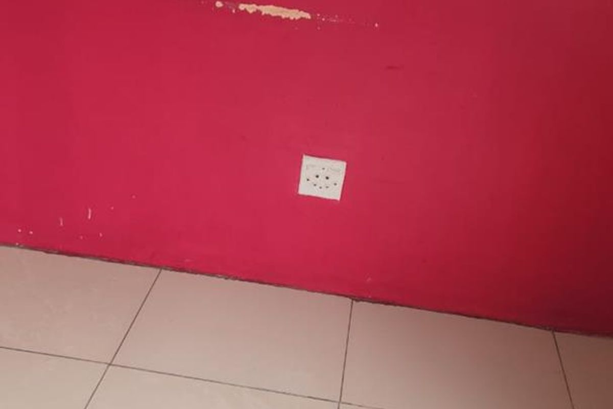 A view of a room interior featuring tiled flooring and a red painted wall with a visible electrical outlet.