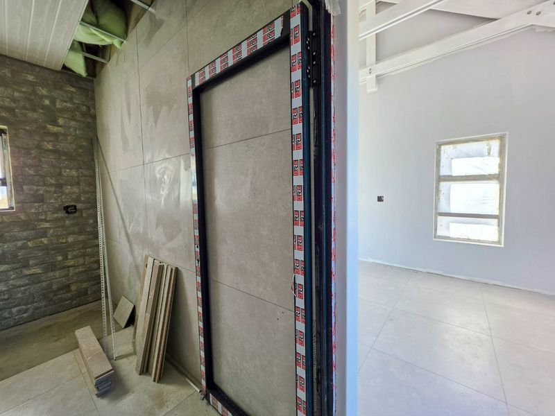 An interior space under construction featuring large format floor tiles, a stone veneer feature wall, and an installed aluminium door frame.