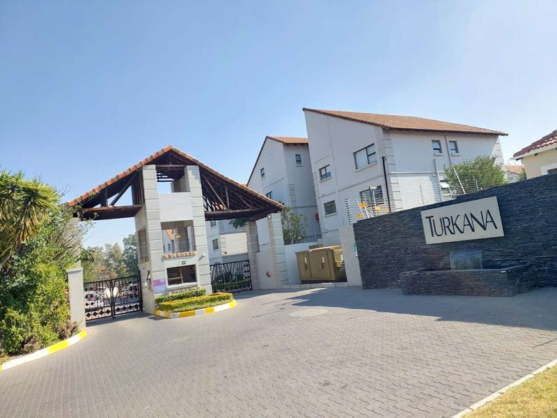 The entrance to Turkana apartment complex featuring a secure gatehouse, paved driveway, and a prominent stone signage wall.