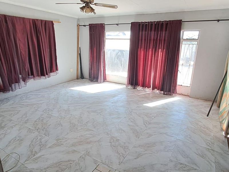 An empty living room featuring tiled flooring, a ceiling fan, and large windows with curtain rods, offering a blank canvas for interior design.