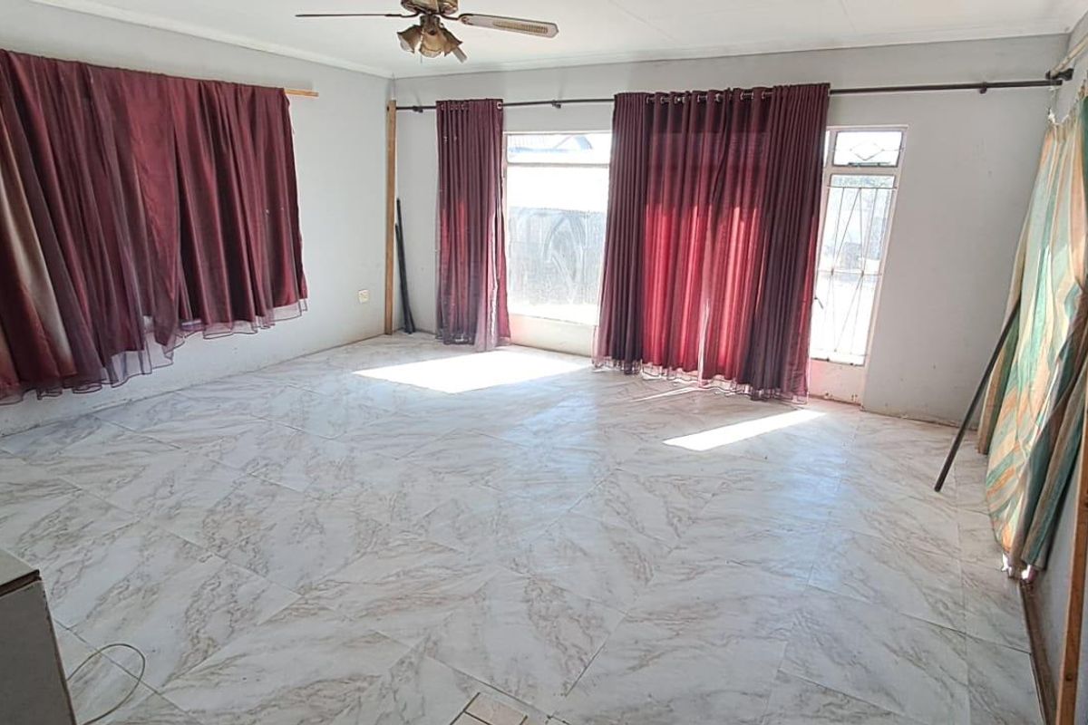 An empty living room featuring tiled flooring, a ceiling fan, and large windows with curtain rods, offering a blank canvas for interior design.