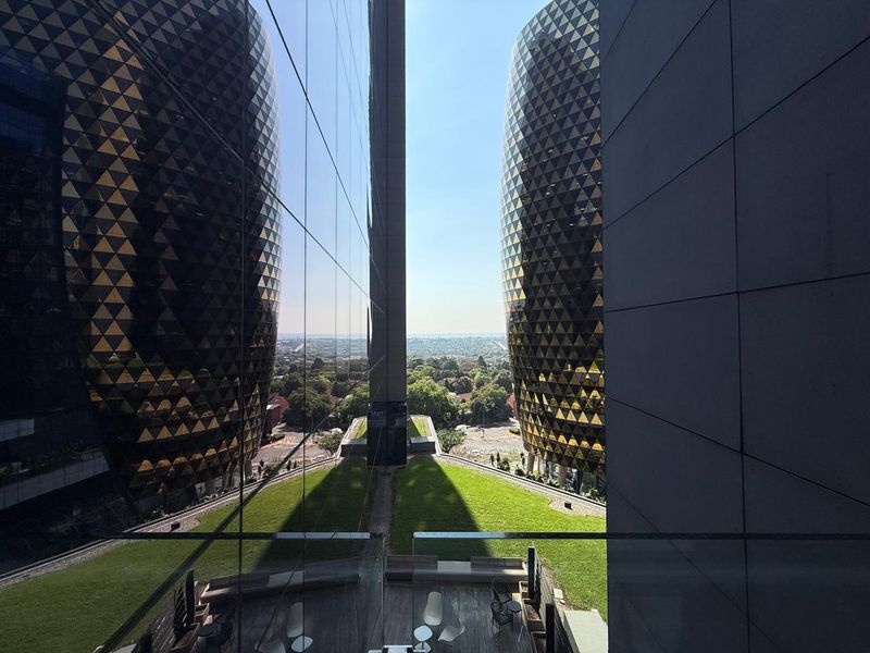 A high-angle view from an office building looking out over a landscaped terrace and surrounding urban landscape between two modern architectural towers.
