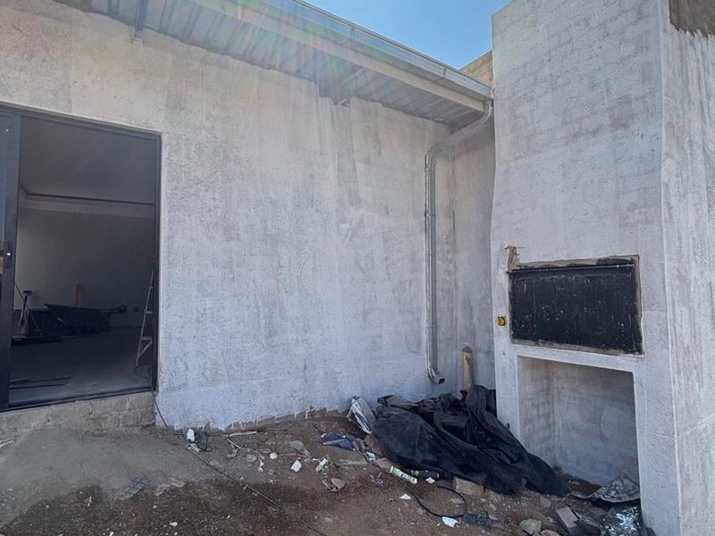 Rear exterior view of the property featuring a built-in braai and unfinished wall surfaces, currently undergoing construction and landscaping.