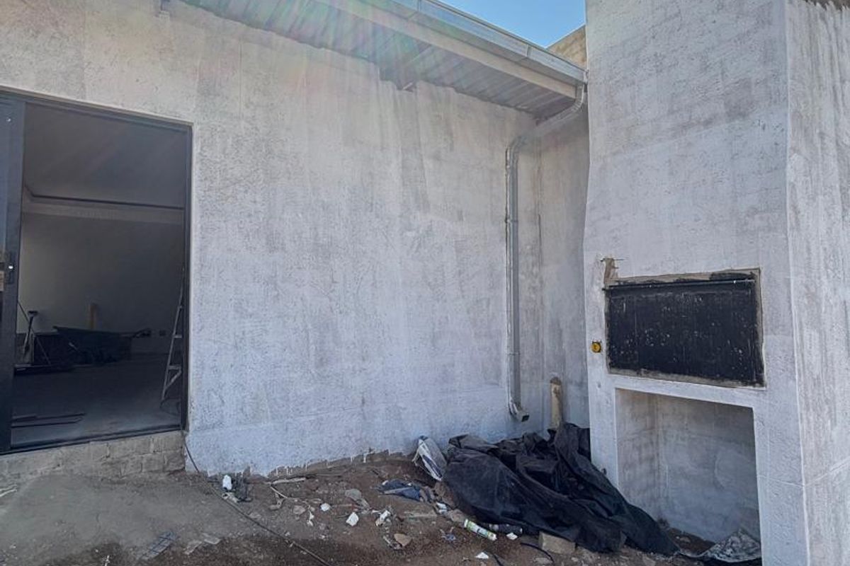 Rear exterior view of the property featuring a built-in braai and unfinished wall surfaces, currently undergoing construction and landscaping.