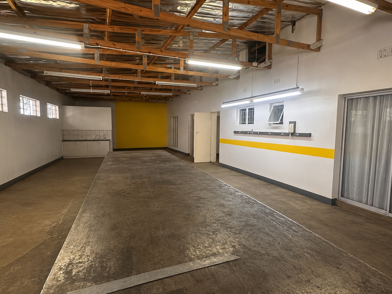 Spacious utility area featuring exposed timber roof trusses, concrete flooring, a small kitchenette, and sliding glass doors providing natural light.