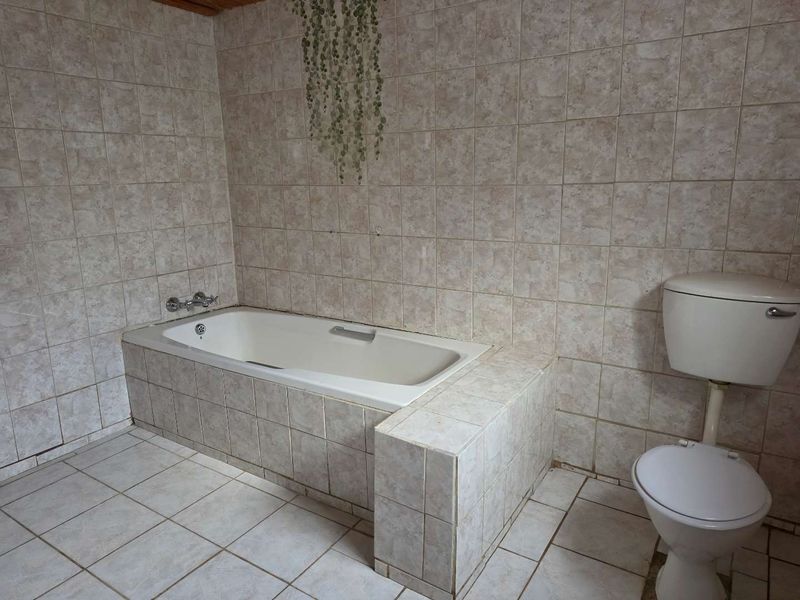 A dated bathroom featuring a built-in bathtub and toilet with full-height ceramic wall tiling and tiled flooring.