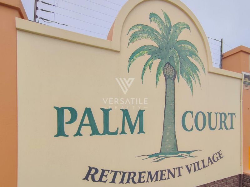 Entrance signage for Palm Court Retirement Village, featuring a painted palm tree mural on a solid boundary wall with integrated electric fencing.