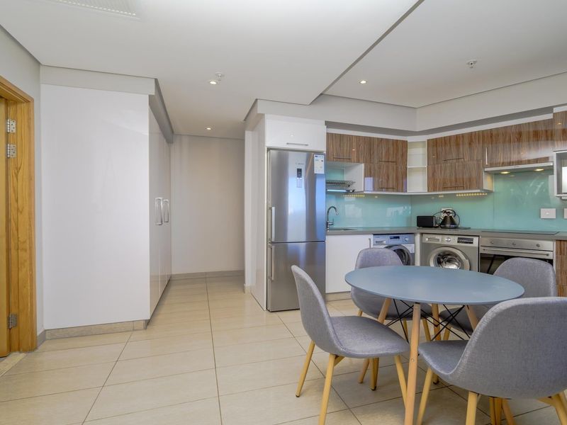 Modern open-plan kitchen featuring sleek wood-grain cabinetry, glass splashbacks, integrated appliances, and tiled flooring, seamlessly flowing into the dining area.