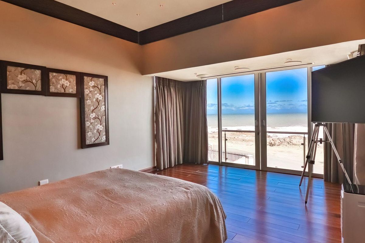 Spacious bedroom featuring rich hardwood flooring, recessed ceiling detailing, and floor-to-ceiling glass sliding doors offering expansive ocean views.