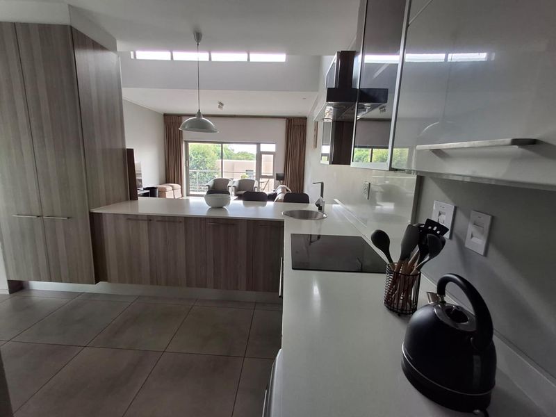 Modern open-plan kitchen featuring sleek cabinetry, stone countertops, and integrated appliances, flowing seamlessly into a bright living area with access to a balcony.