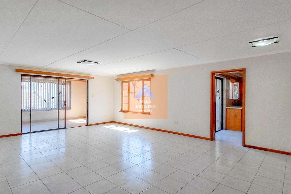 Spacious, empty living area featuring neutral tiled flooring, wooden window frames, and access to an adjoining balcony through sliding glass doors.