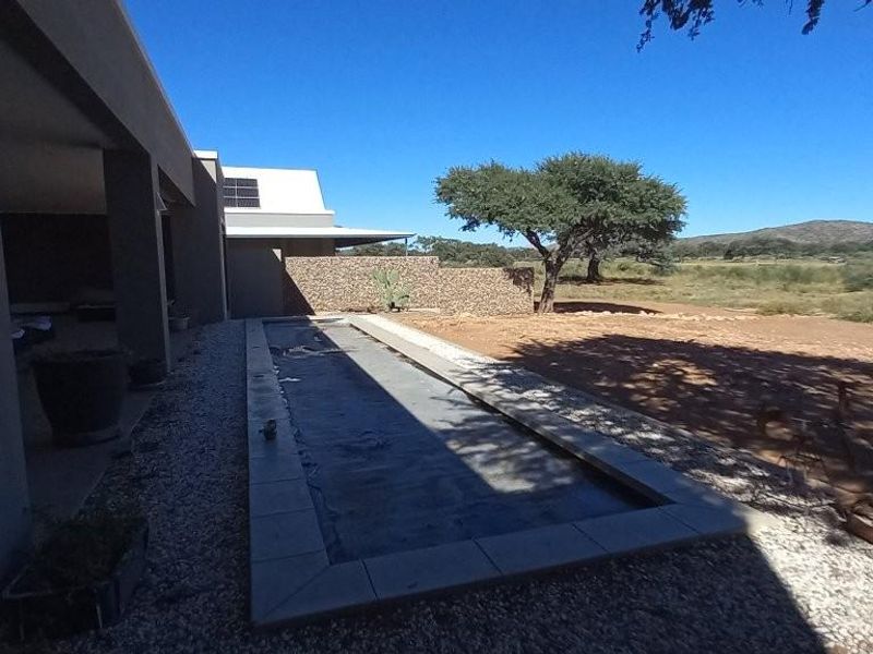 A rectangular swimming pool set alongside a covered patio area, featuring a stone retaining wall and expansive views of the surrounding natural landscape.