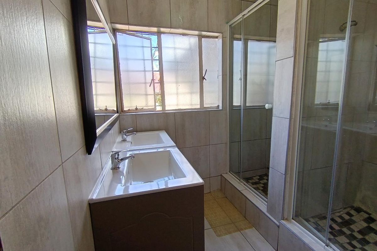 A functional bathroom featuring a double vanity unit, a glass-enclosed shower, and neutral wall and floor tiling.
