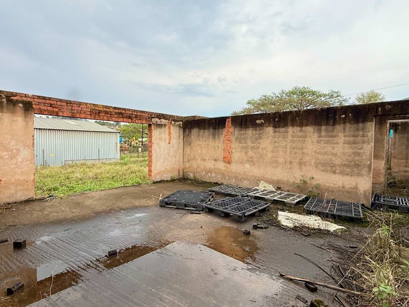 An open-air structure featuring weathered brick masonry walls and a concrete slab floor, showing significant signs of wear and exposure to the elements.