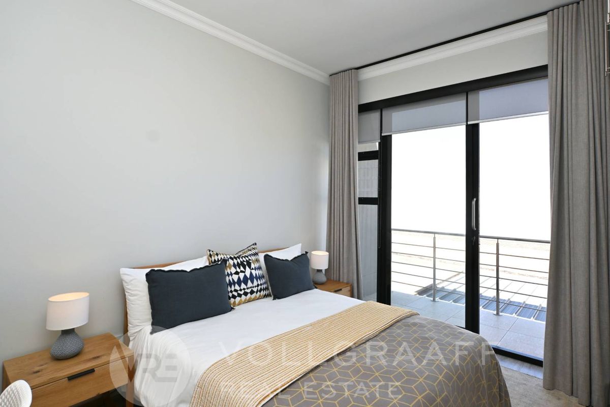 A bright bedroom featuring neutral walls, crown molding, and large sliding glass doors that open onto a private balcony.