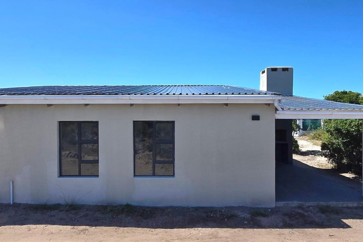 A side view of a single-story house featuring a metal roof, chimney, and a covered patio area with an integrated outdoor fireplace.