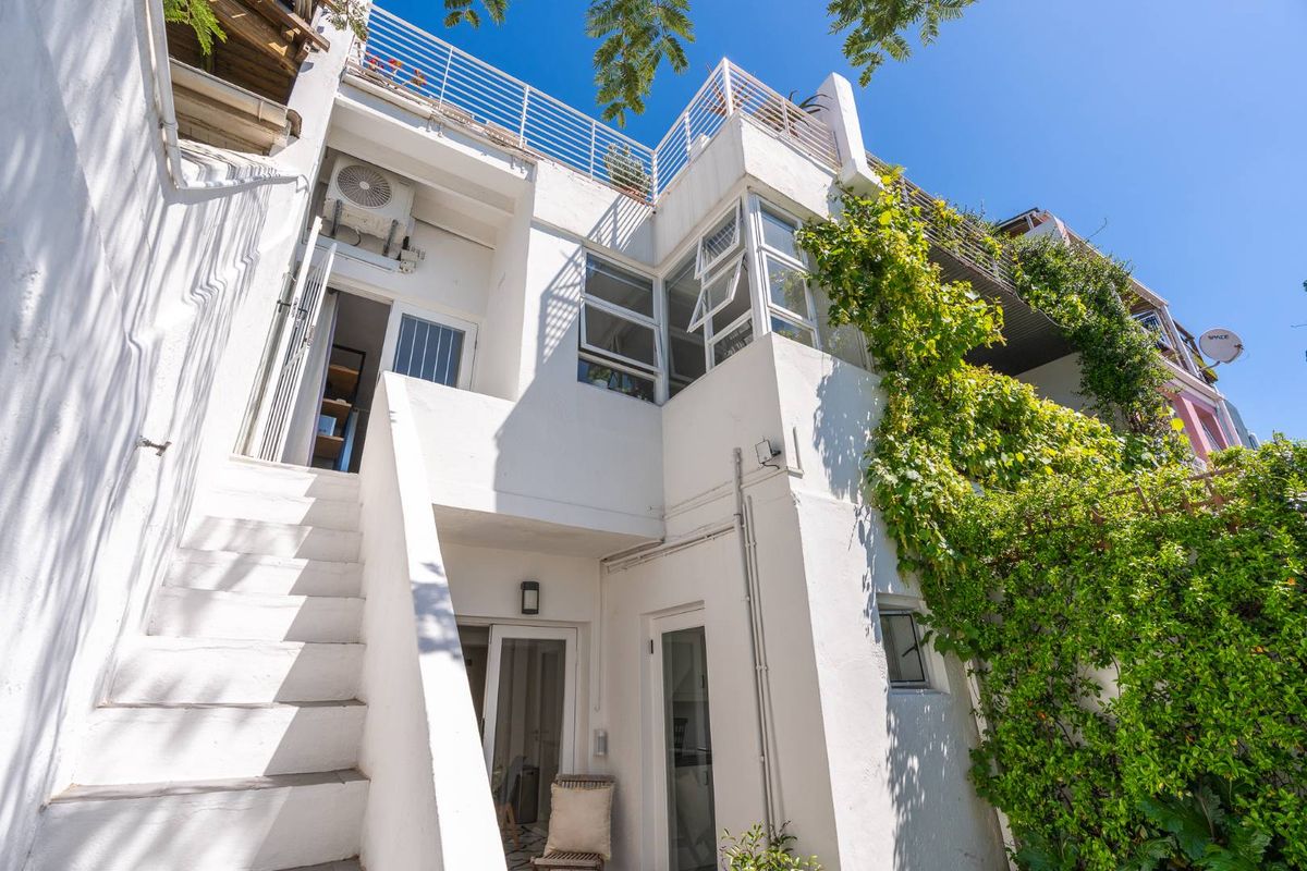 Rear exterior view of a multi-level property featuring white rendered walls, an external staircase, and an upper-level balcony with metal railings.