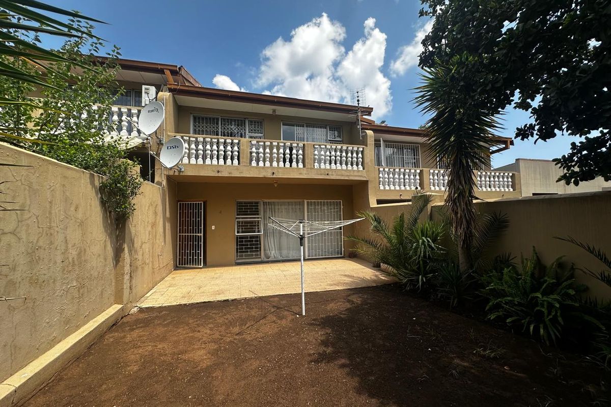 Rear view of the townhouse featuring a tiled patio, upper-level balcony with balustrades, and a private garden area enclosed by boundary walls.