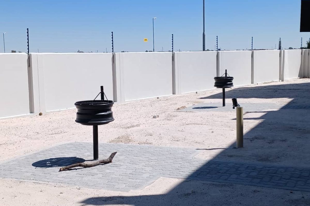 Rear outdoor area featuring a precast boundary wall with electric fencing, paved sections, and built-in braai stands, currently awaiting landscaping.