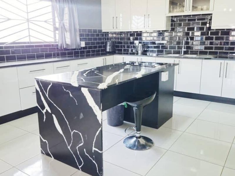 Modern kitchen featuring a striking black and white marble-look island, high-gloss white cabinetry, and a contrasting black subway tile backsplash.