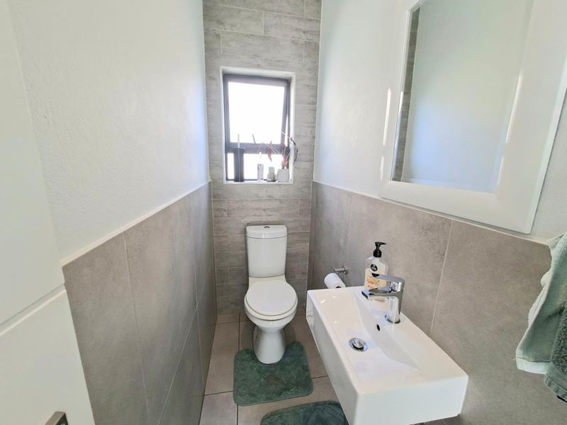 A modern, compact guest bathroom featuring neutral grey wall tiles, a wall-mounted basin with a mixer tap, and a toilet.