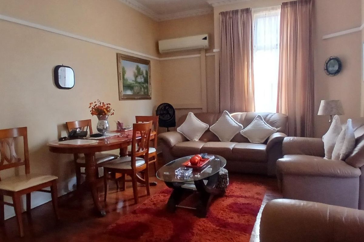 A comfortable living and dining area featuring hardwood flooring, crown molding, and a wall-mounted split-system air conditioner.