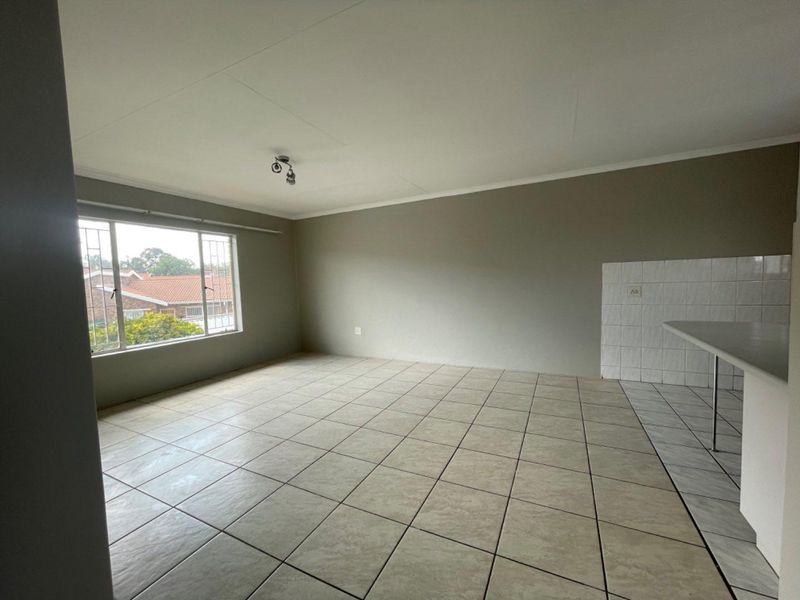 An empty open-plan living area featuring tiled flooring, a breakfast counter with tiled splashback, and large windows with security bars.